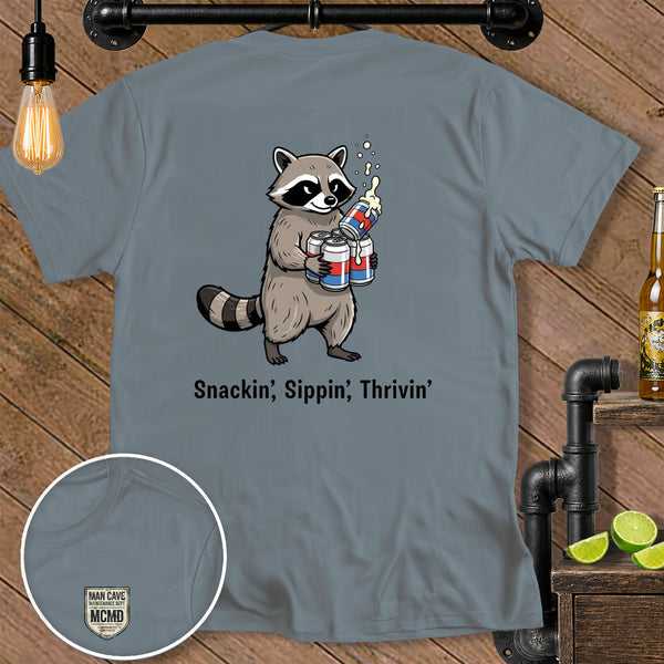 Cartoon raccoon holding four beer cans with foam, text "Snackin', Sippin', Thrivin'".
