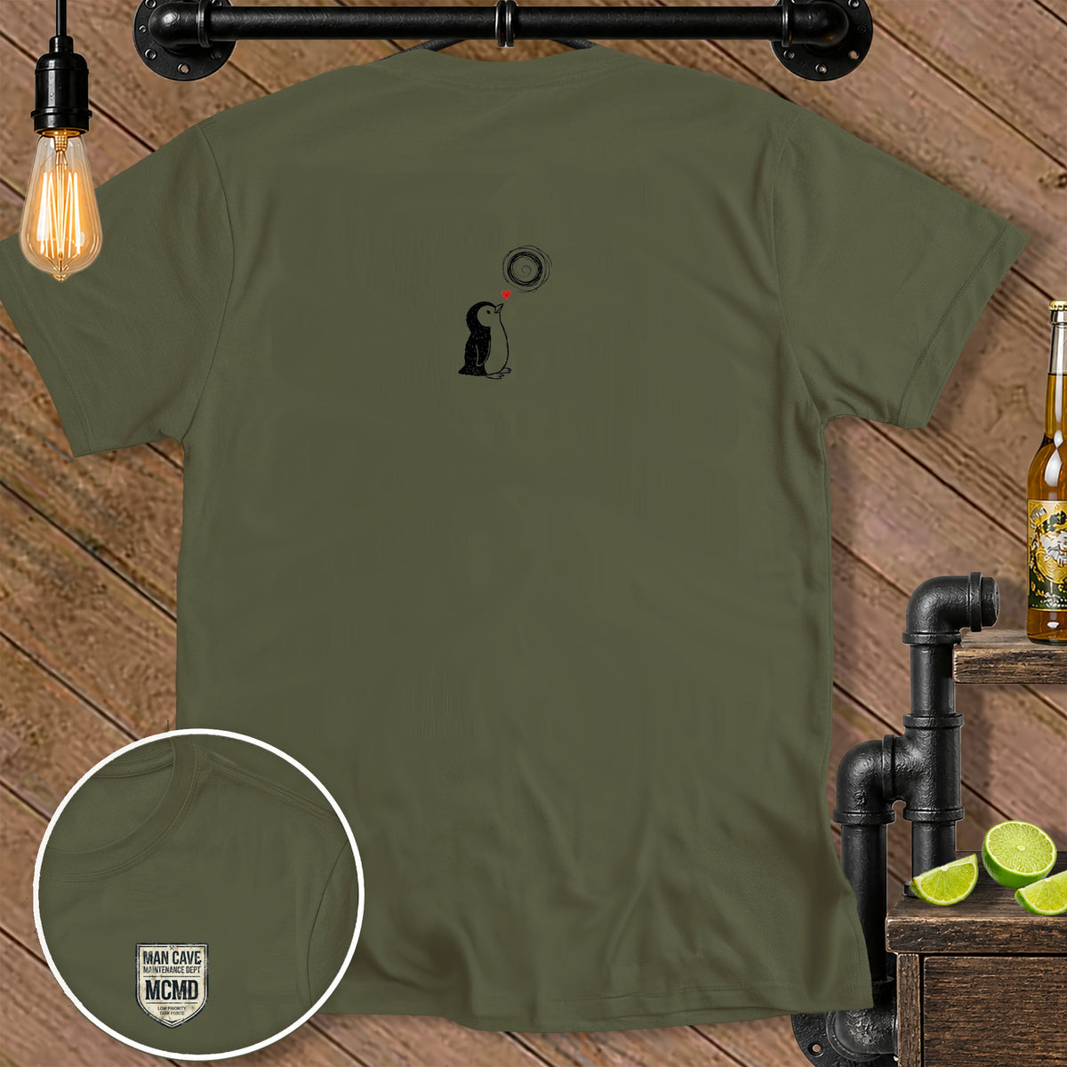Olive green t-shirt with penguin graphic and "MAN CAVE MCMD" chest logo.