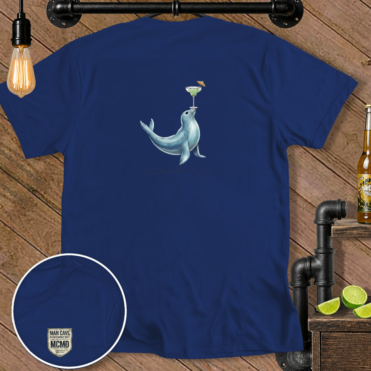 Blue t-shirt with a seal balancing a cocktail and text "Sealing the Buzz".