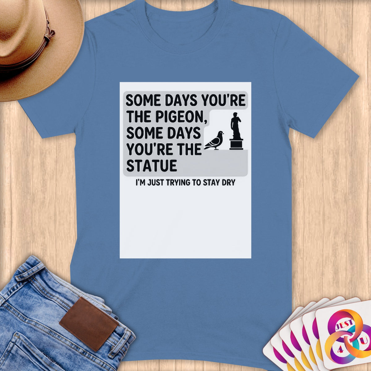 Blue t-shirt with text: "Some days you're the pigeon, some days you're the statue. I'm just trying to stay dry."