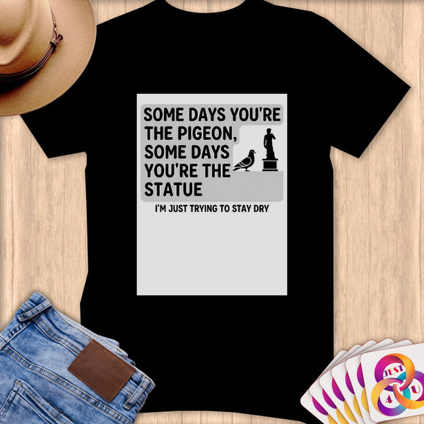 Black t-shirt with text "Some days you're the pigeon, some days you're the statue. I'm just trying to stay dry."