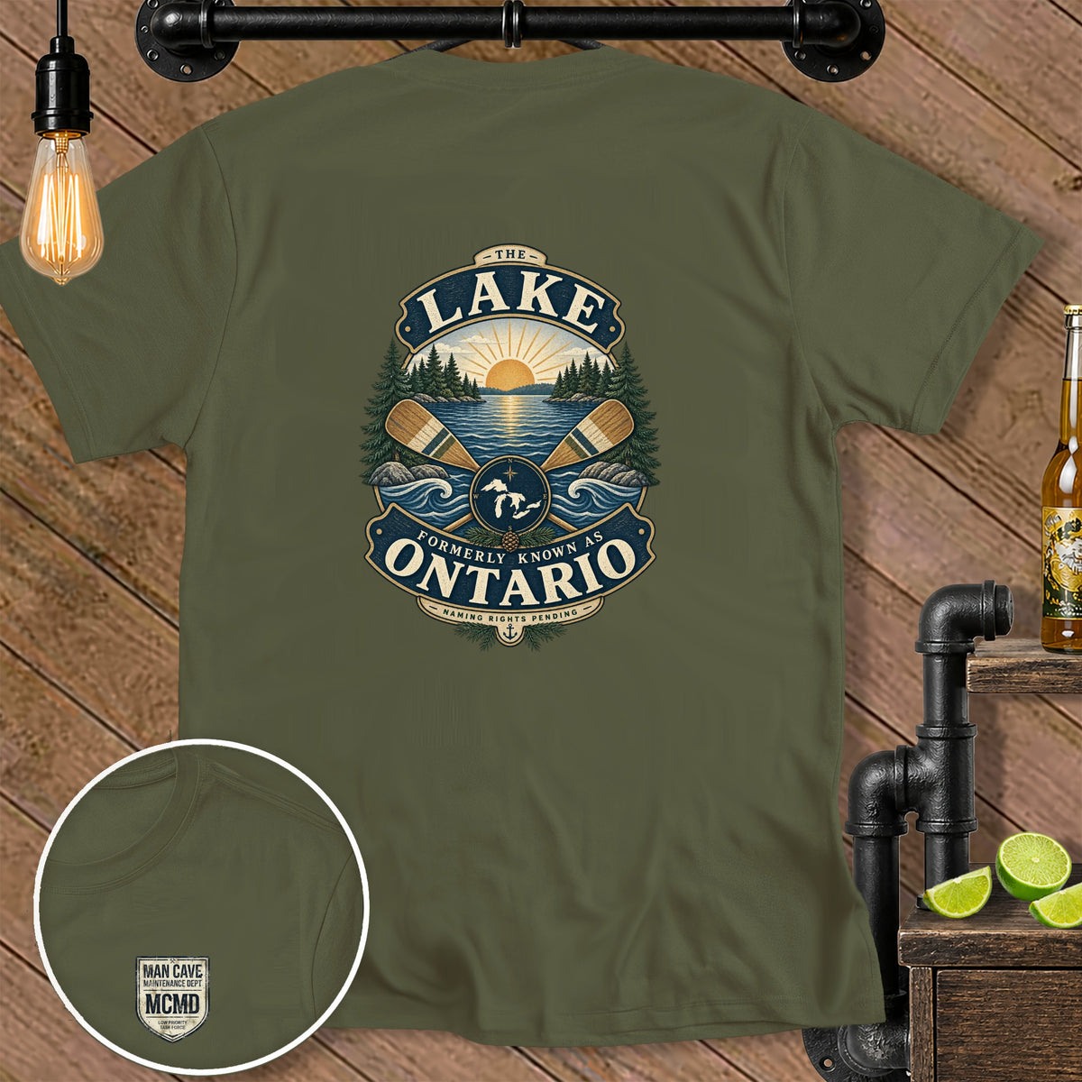 Green t-shirt with a badge graphic featuring a lake, sun, trees, and oars.