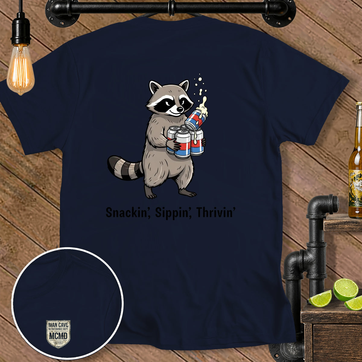 Navy t-shirt with cartoon raccoon holding four cans of soda and text "Snackin', Sippin', Thrivin'".